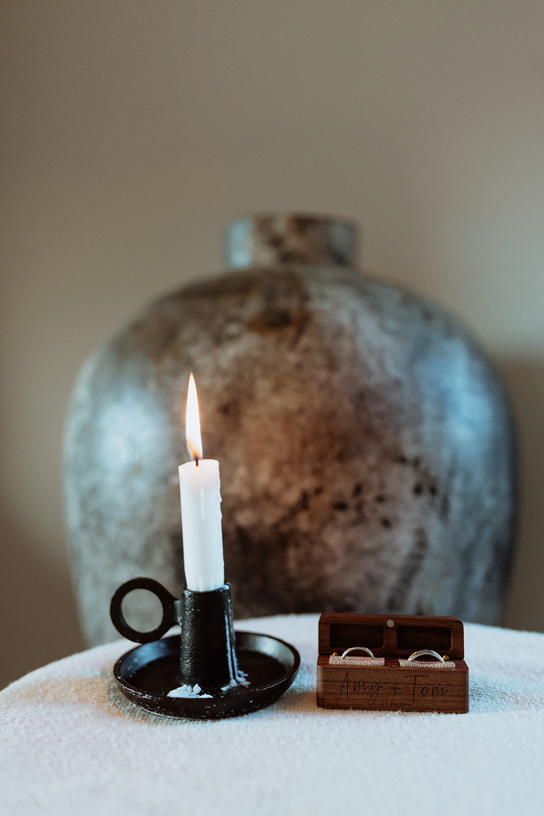 Close-up of wedding rings resting next to a glowing candle, adding a romantic and intimate touch to the bridal details.
