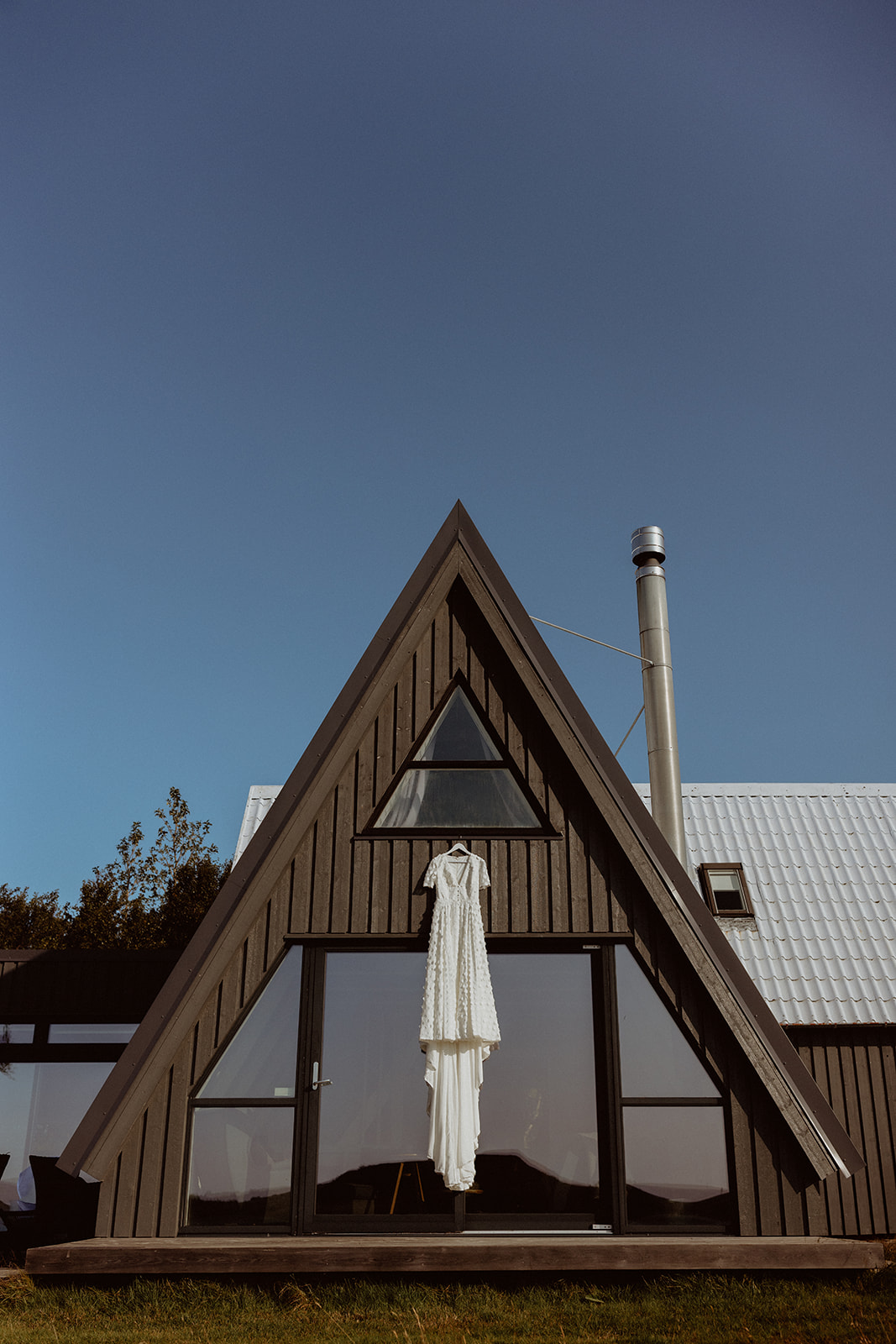 Amy’s wedding dress hanging from the A-frame of Eirð Retreat, showcasing its delicate design and soft texture against the serene Icelandic backdrop.