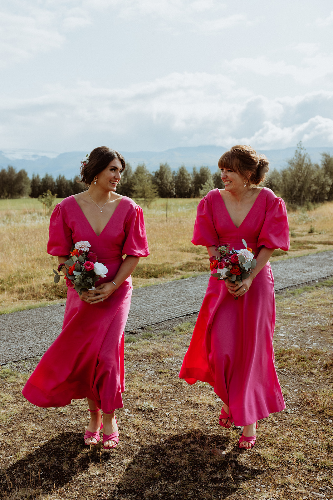 Bridesmaids in pink dresses walking towards the stunning Gluggafoss waterfall, setting the scene for the bride's Icelandic elopement.