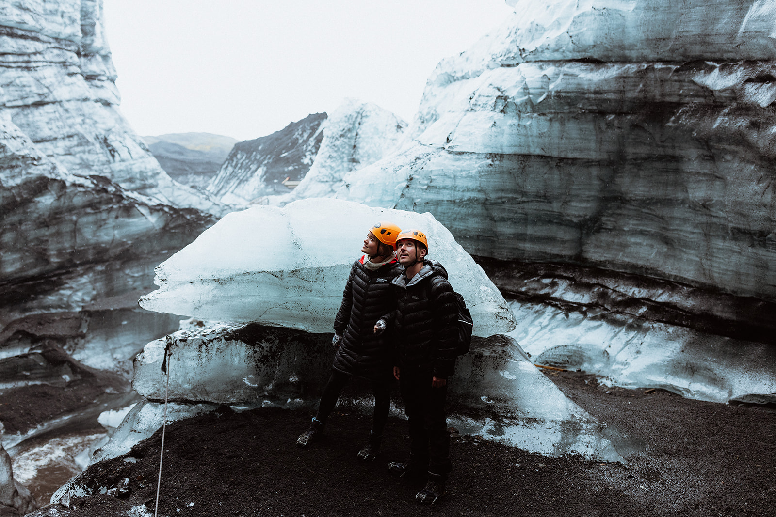 Amy and Tom standing together in front of a dramatic ice crevasse on Katla glacier, with sharp blue ice contrasting against the snow.