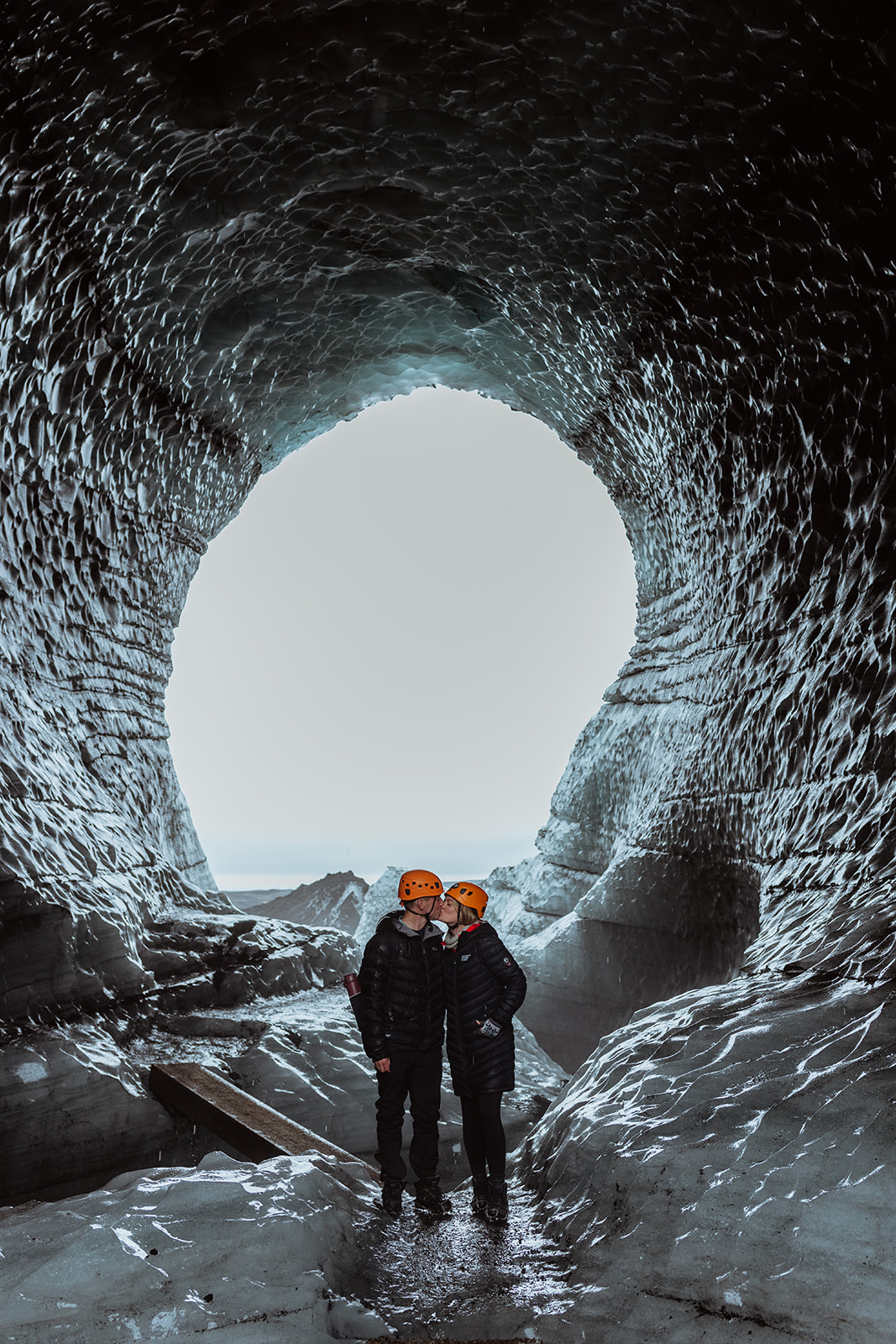 Amy and Tom exploring the dark, crystalline ice cave of Katla glacier, with shimmering blue ice surrounding them.