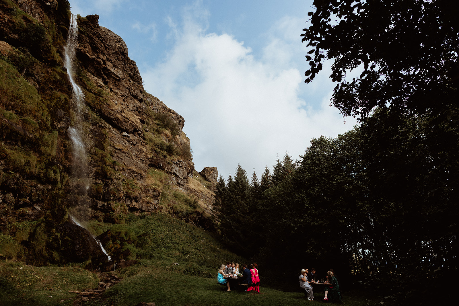 Wide shot of the waterfall at Thornsteins Grove with a picturesque picnic setup, part of the Iceland elopement celebration.