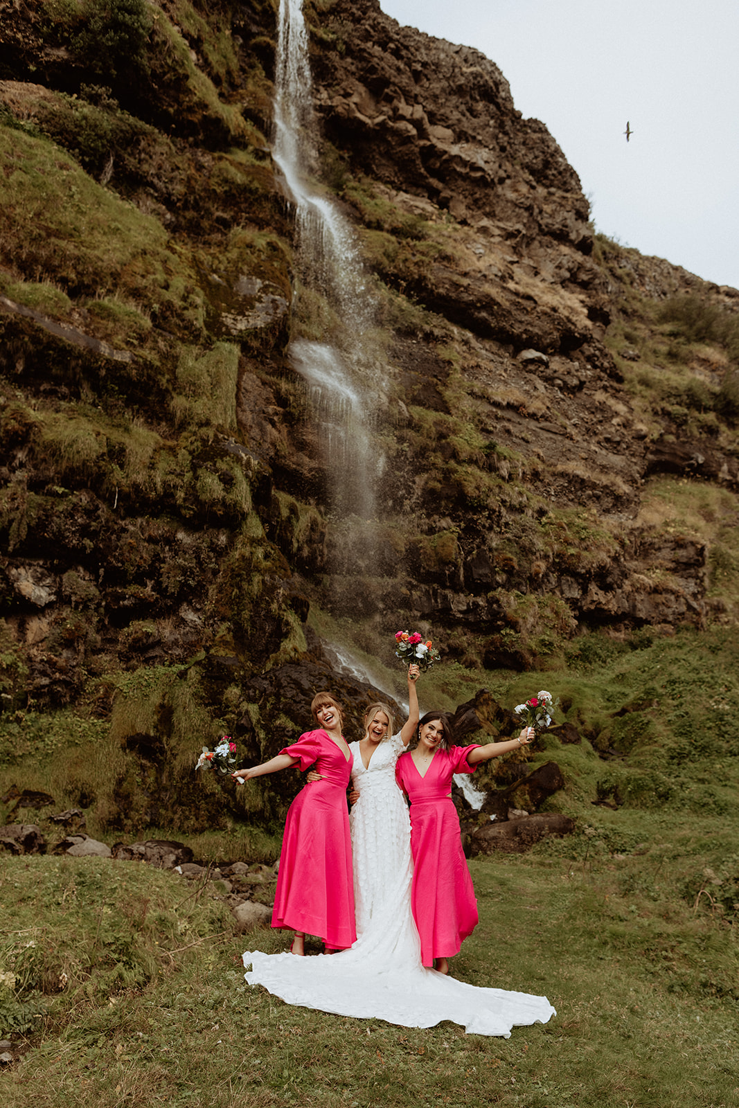 Bride and bridesmaids posing beneath the stunning waterfall at Thornsteins Grove during their Iceland elopement.