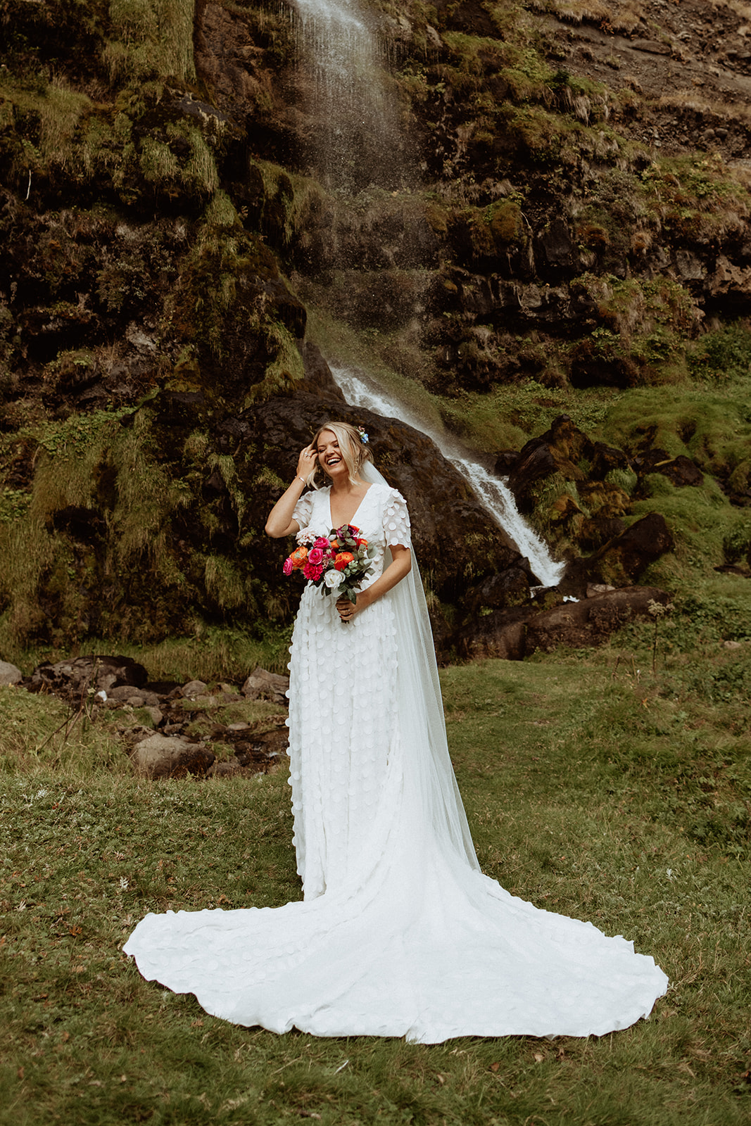 Bride standing gracefully in front of the cascading waterfall at Thornsteins Grove during her Iceland elopement