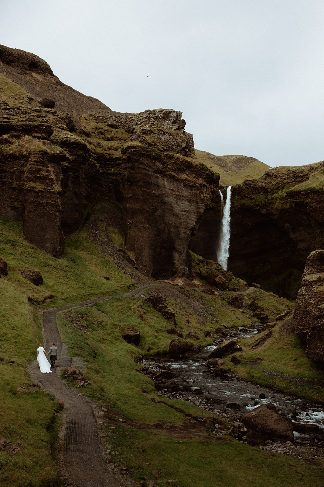 Couple sharing a quiet moment beneath Kvernufoss waterfall in Iceland, capturing their love against the dramatic backdrop