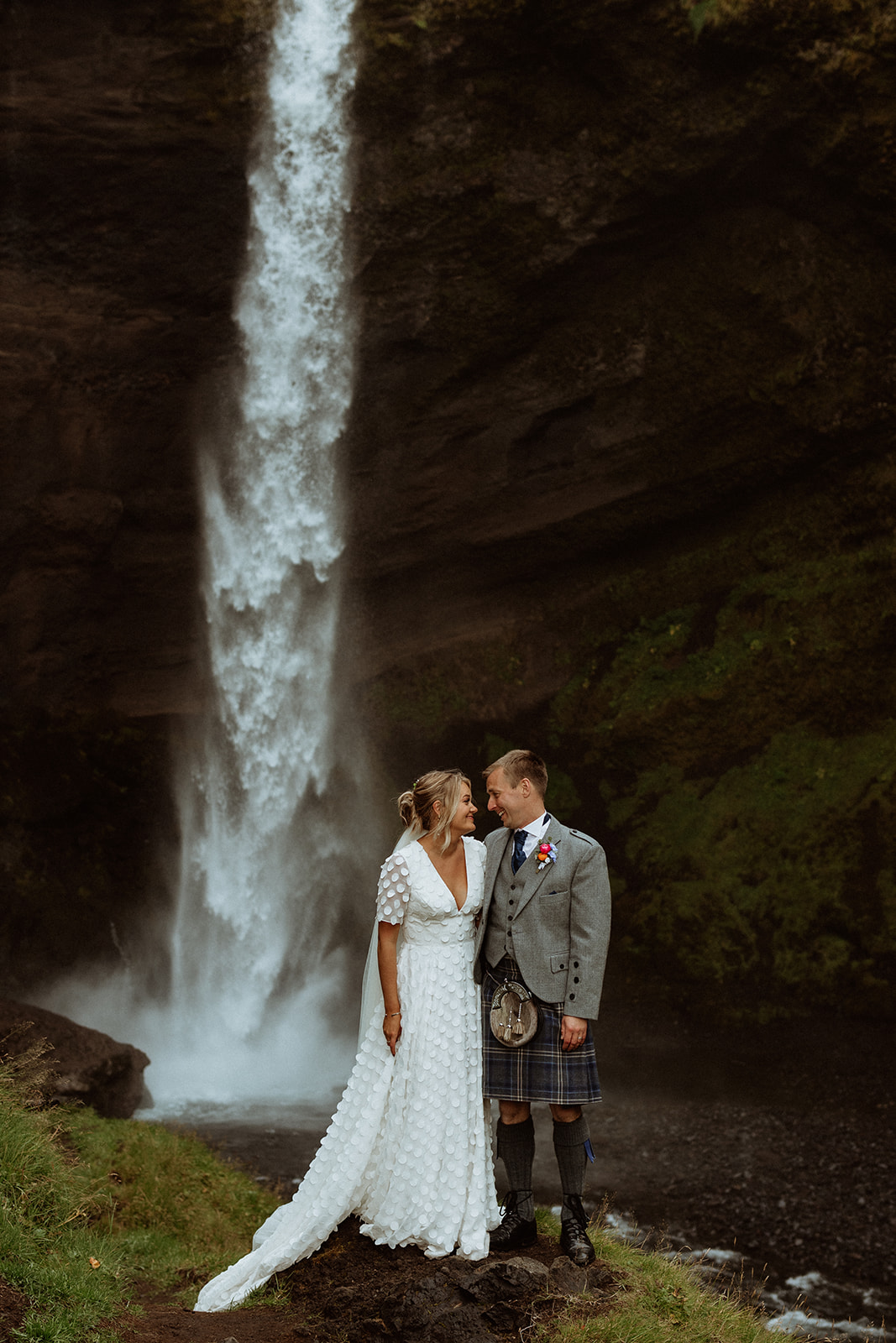 Newlyweds embrace in front of Kvernufoss waterfall, a stunning location for their Icelandic adventure elopement.