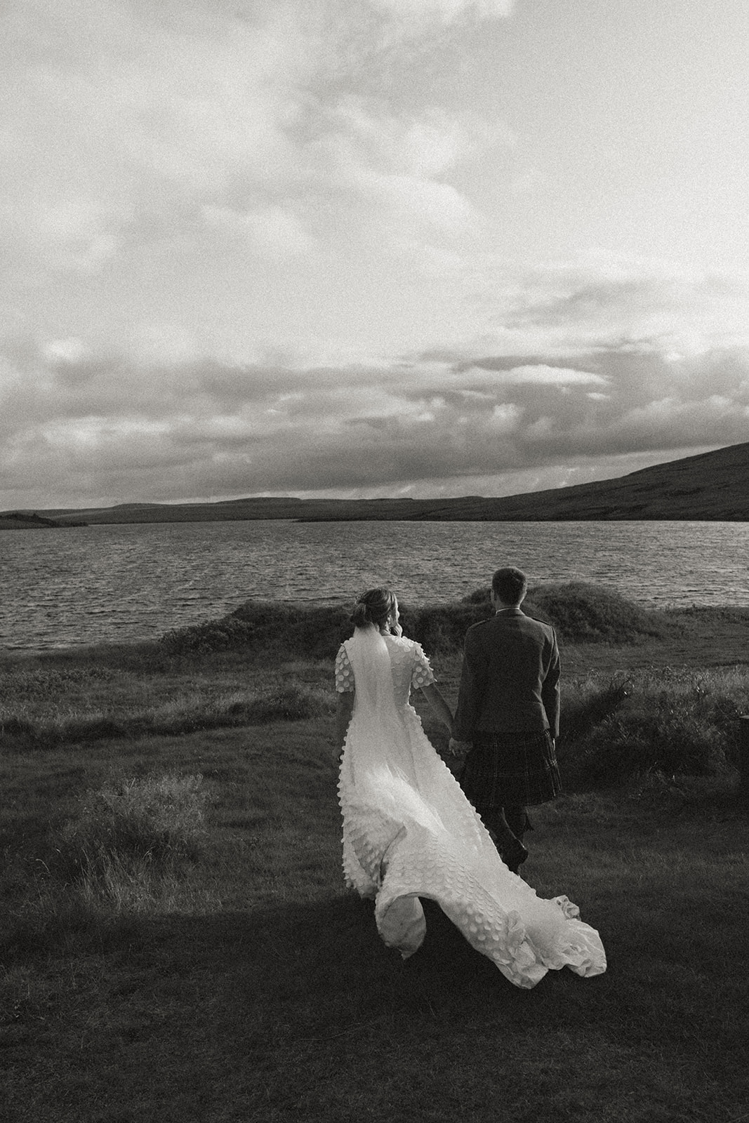 Newlywed couple standing by the serene waters of Eirð Retreat, surrounded by Iceland's natural beauty, capturing a quiet moment of love and intimacy.