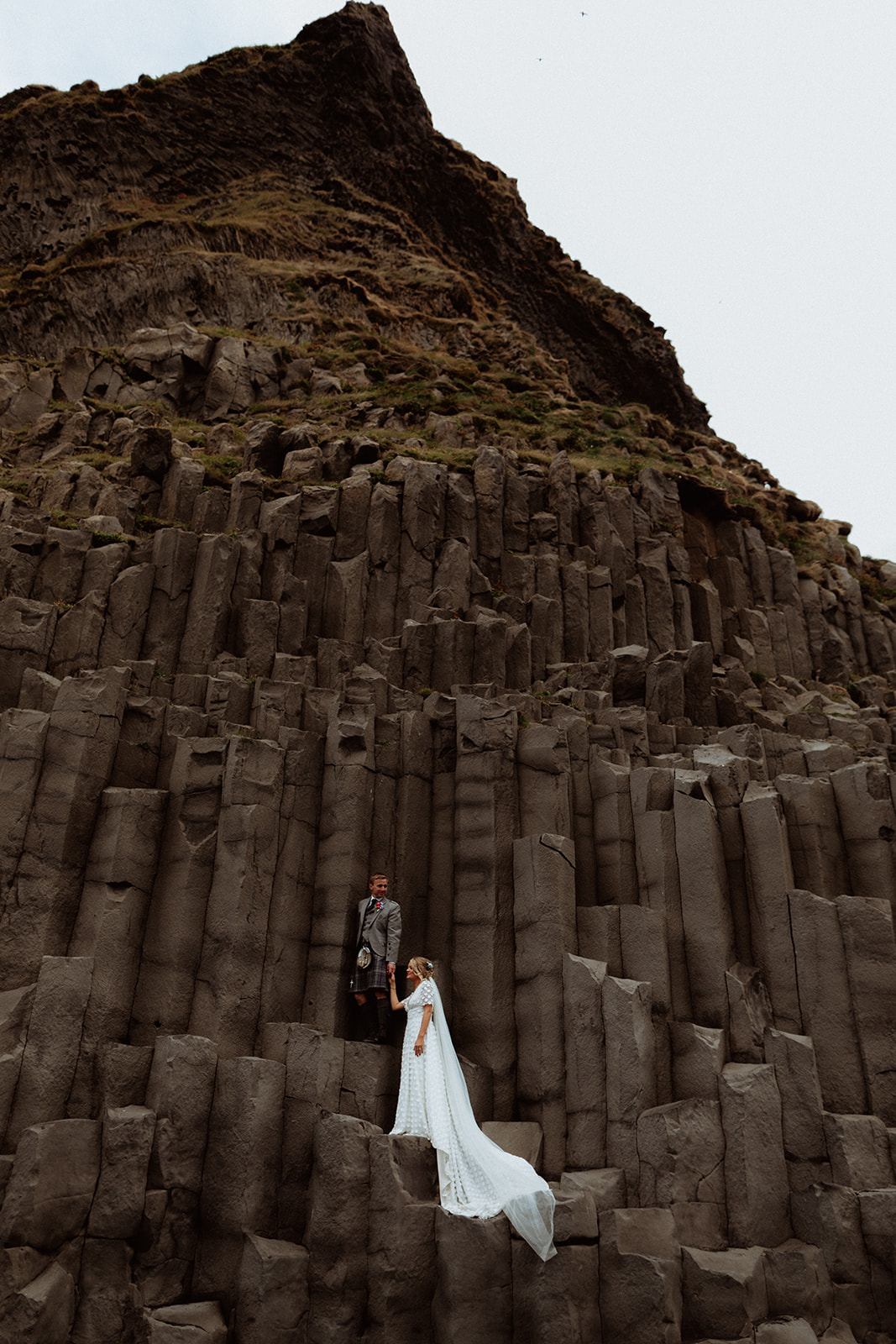 The couple shares a quiet moment at Reynisfjara, surrounded by dramatic basalt columns and the crashing waves of the black sand beach