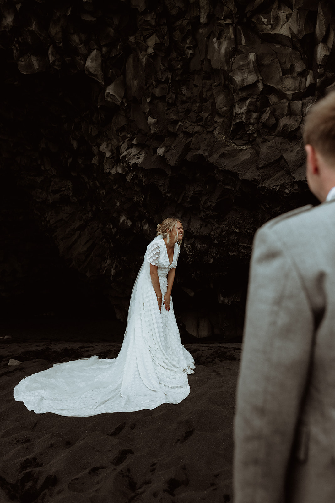 Amy and Tom share a quiet, intimate moment inside the Reynisfjara cave, with the rugged, volcanic rock creating a raw and powerful backdrop.