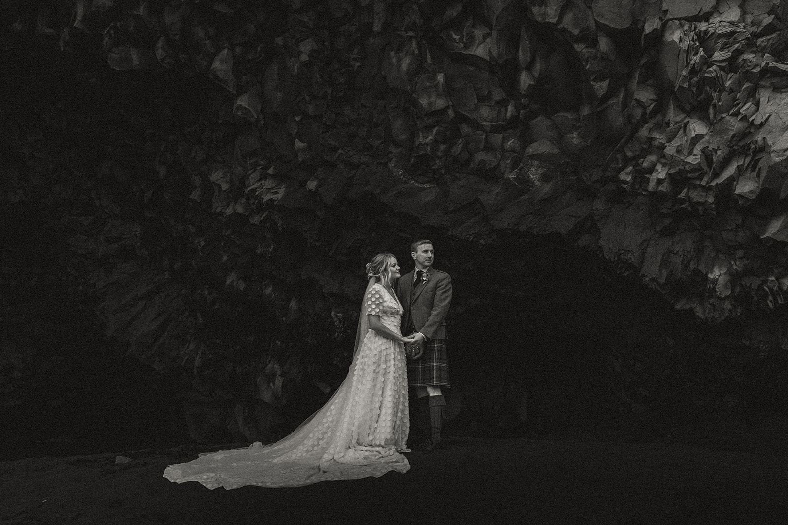 The couple walks hand-in-hand through the stunning Reynisfjara cave, with its volcanic rock and natural beauty surrounding them on their elopement journey.