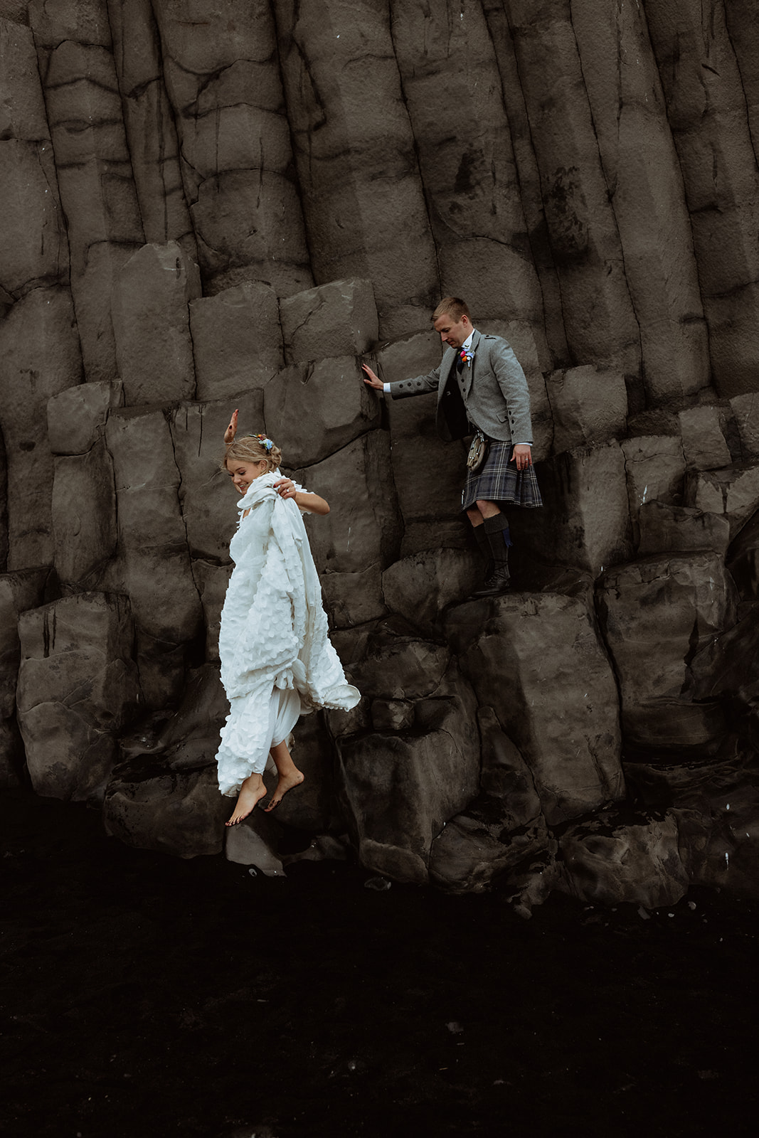 Amy leaps from a basalt column on Reynisfjara Beach, the rugged Icelandic coastline and sea stacks providing a stunning backdrop.