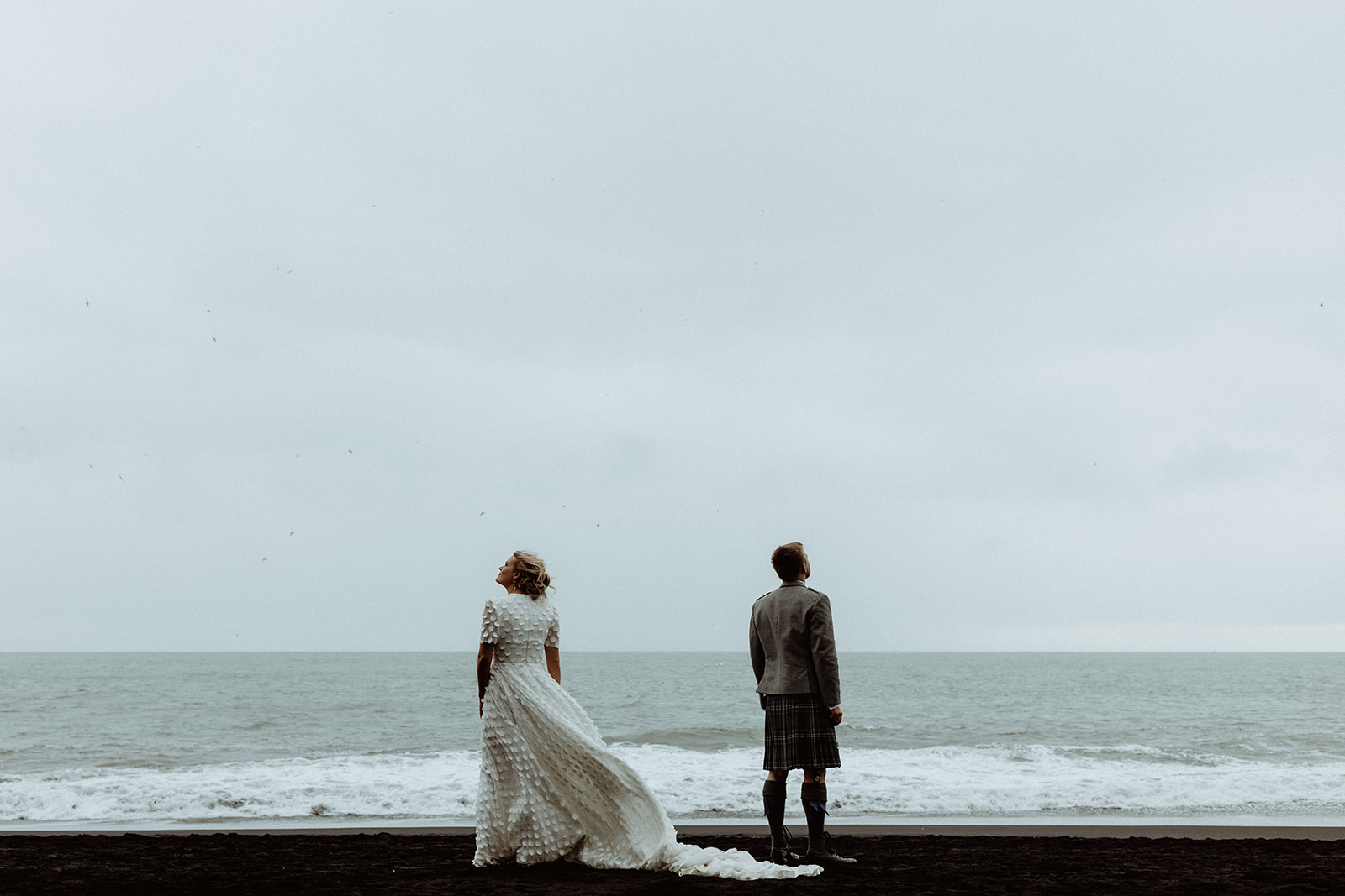 The couple stands side by side, admiring the breathtaking view of Iceland's rugged landscape from a scenic vantage point.