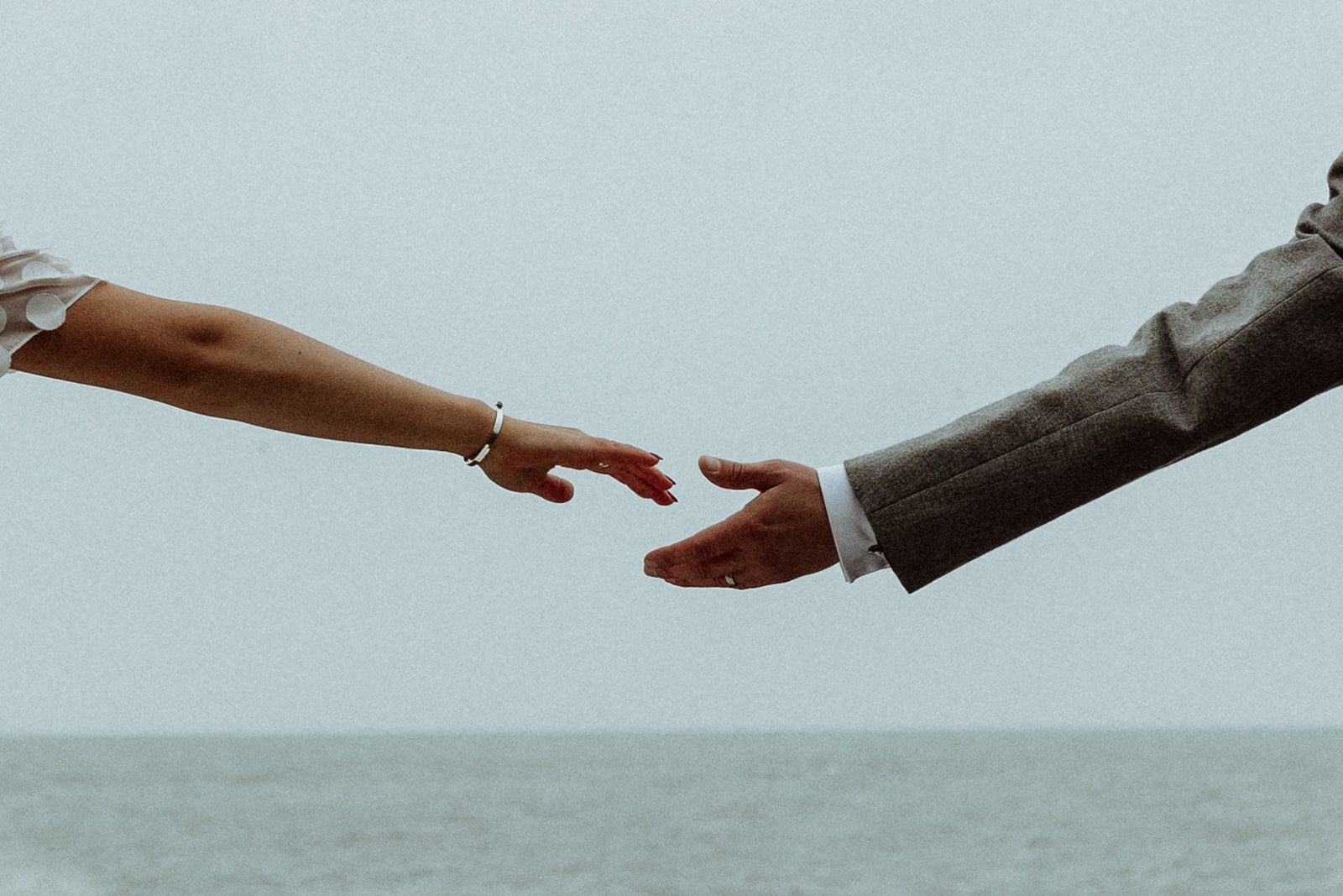 Bride and groom reach for each other’s hands in a quiet moment during their Iceland elopement, surrounded by stunning natural scenery.
