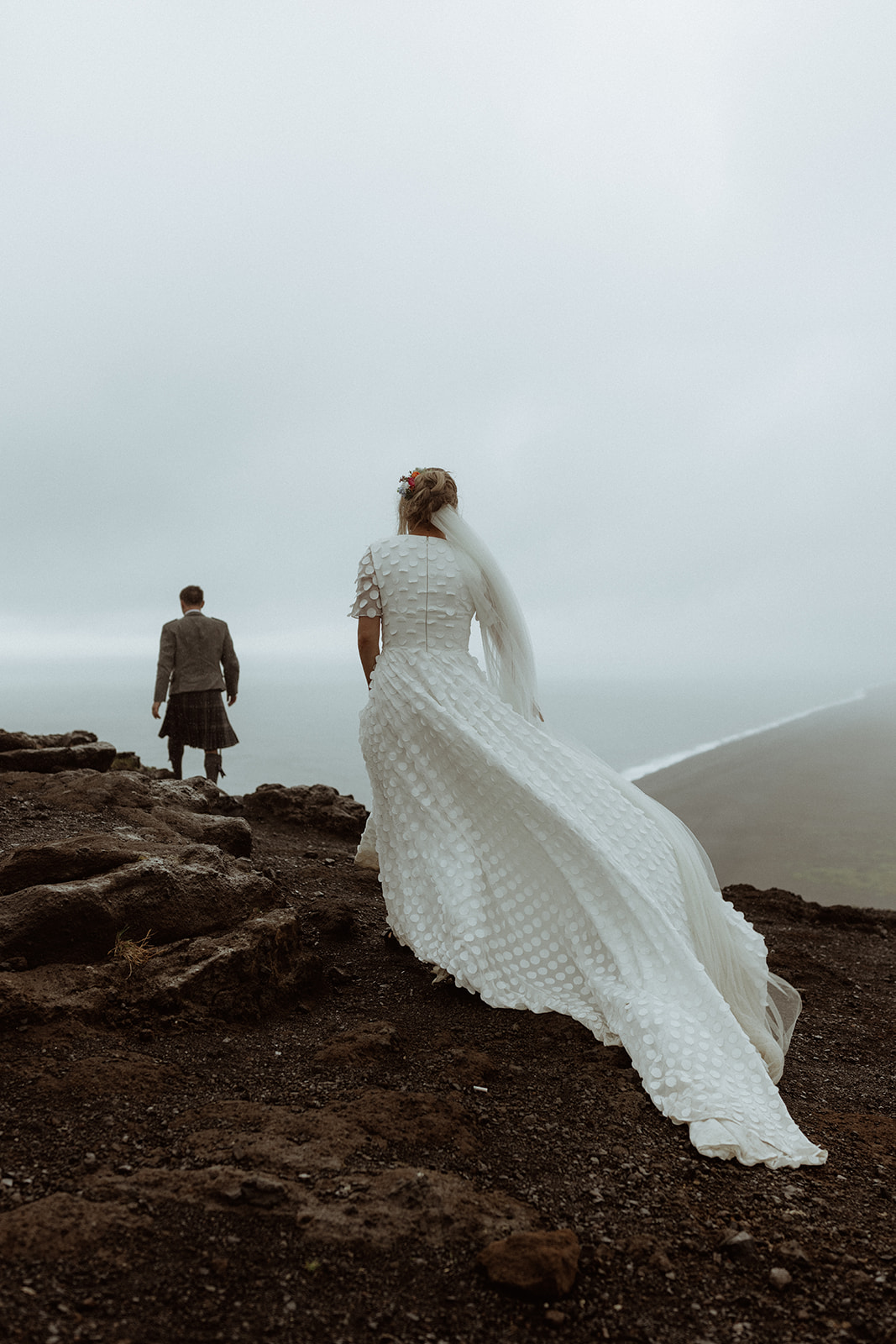 A moment of tranquility as the couple overlooks the cliffs of Dyrhólaey, with the vast Icelandic landscape before them.