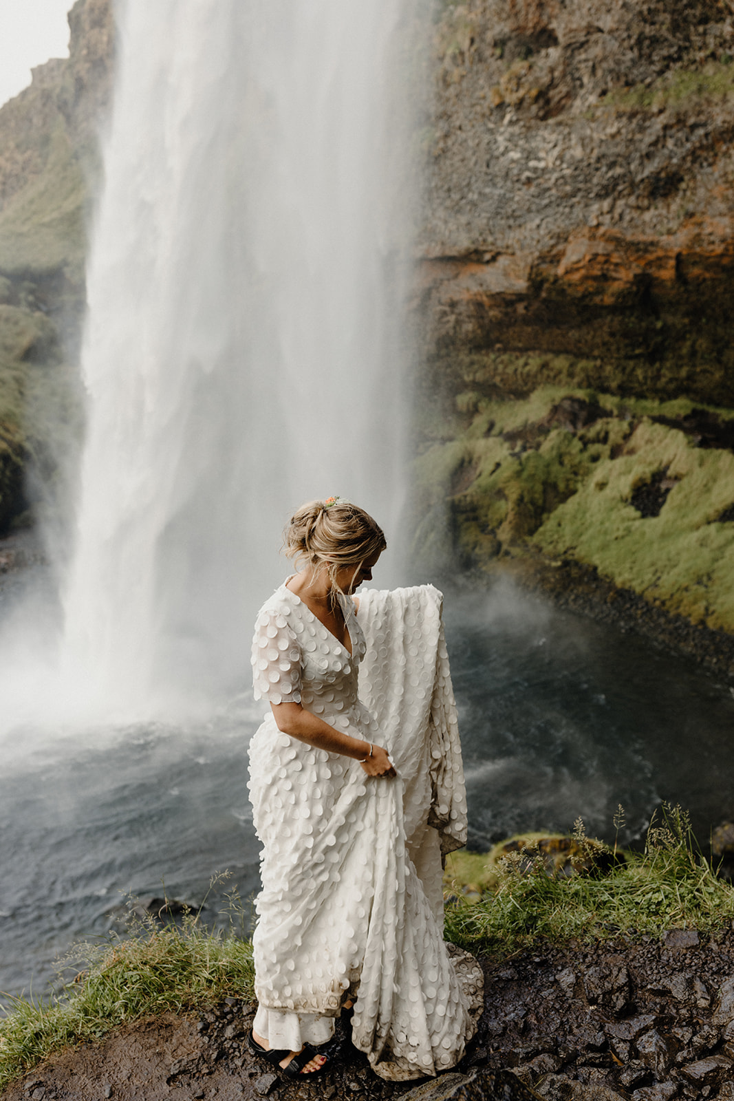 Amy in her wet bridal gown standing in front of Seljalandsfoss waterfall in Iceland, embracing the adventure of her elopement.