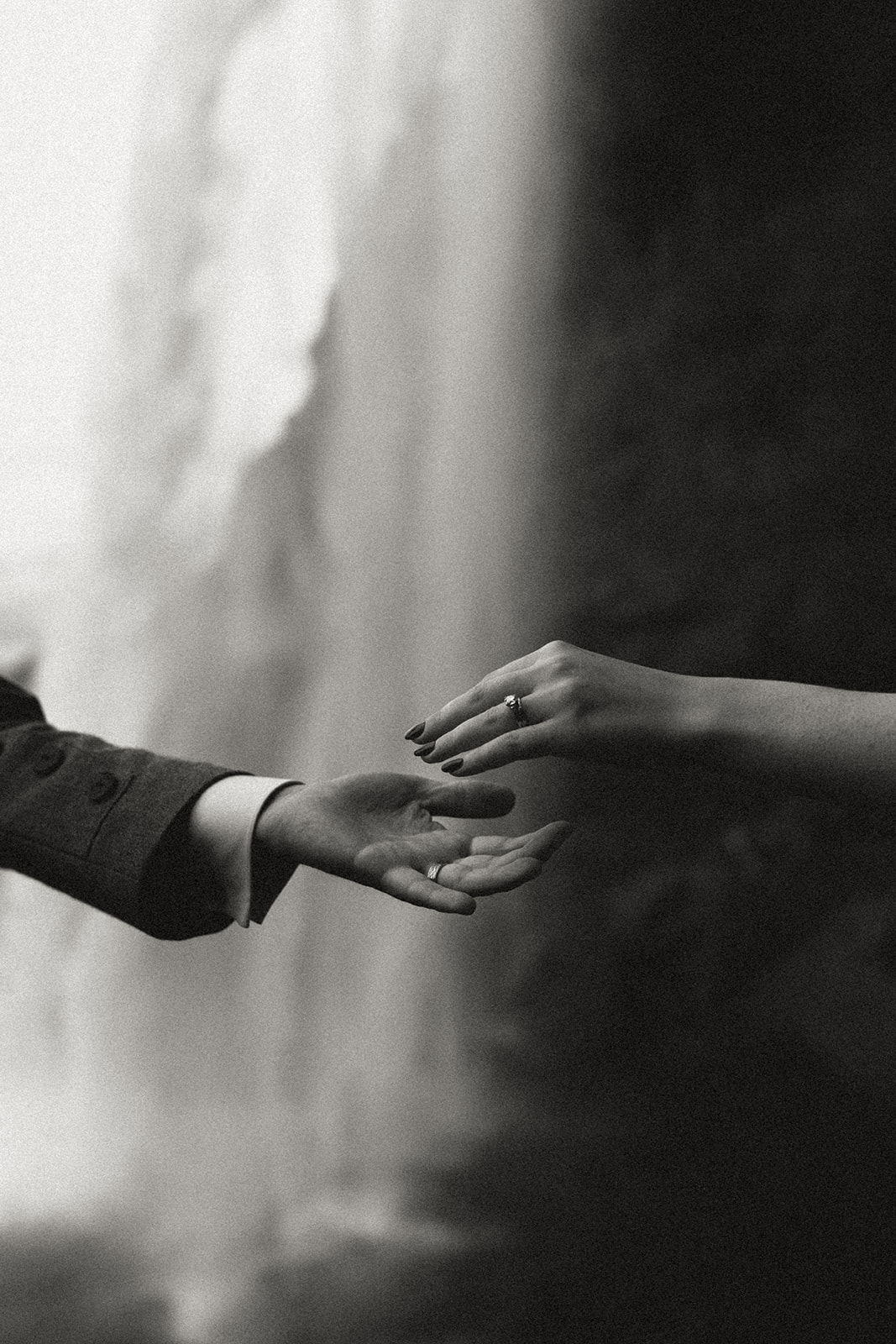 Bride and groom reaching for each other's hands in front of a dramatic waterfall in Iceland during their elopement