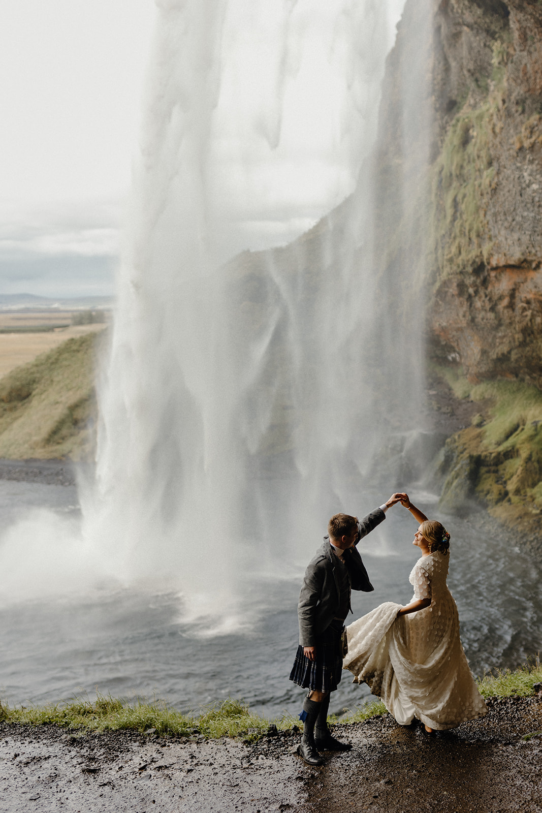 Bride spinning in her wedding dress behind the cascading waters of Seljalandsfoss waterfall in Iceland.