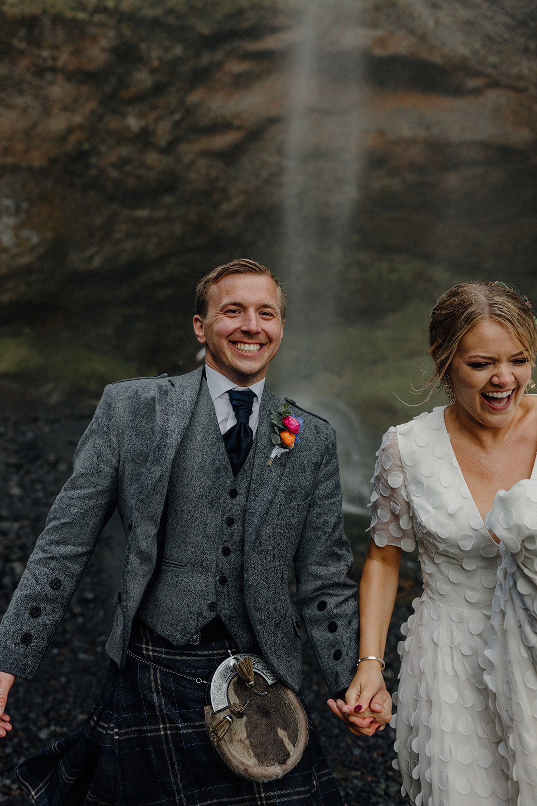 Bride and groom running hand-in-hand under the mist of Seljalandsfoss waterfall during their Iceland elopement