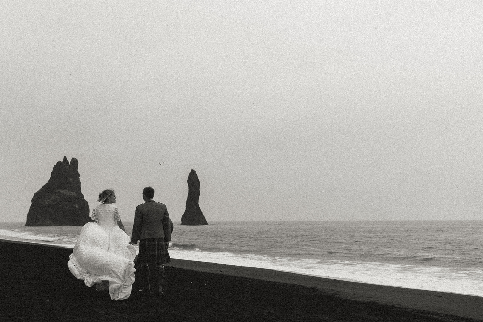 Amy and Tom running together along the striking black sand beach of Reynisfjara, with dramatic cliffs and ocean waves in the background.