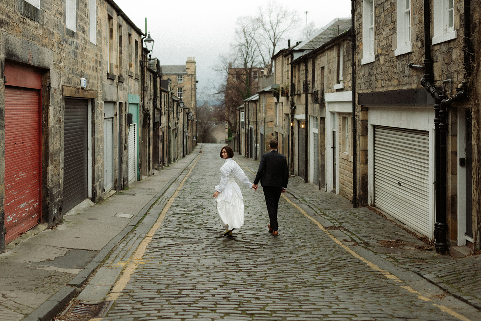 Editorial engagement session capturing a couple walking hand-in-hand through the scenic streets of Edinburgh