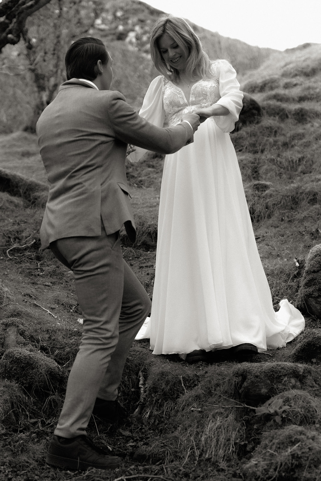 Groom helping bride up a hill during their Isle of Skye elopement adventure