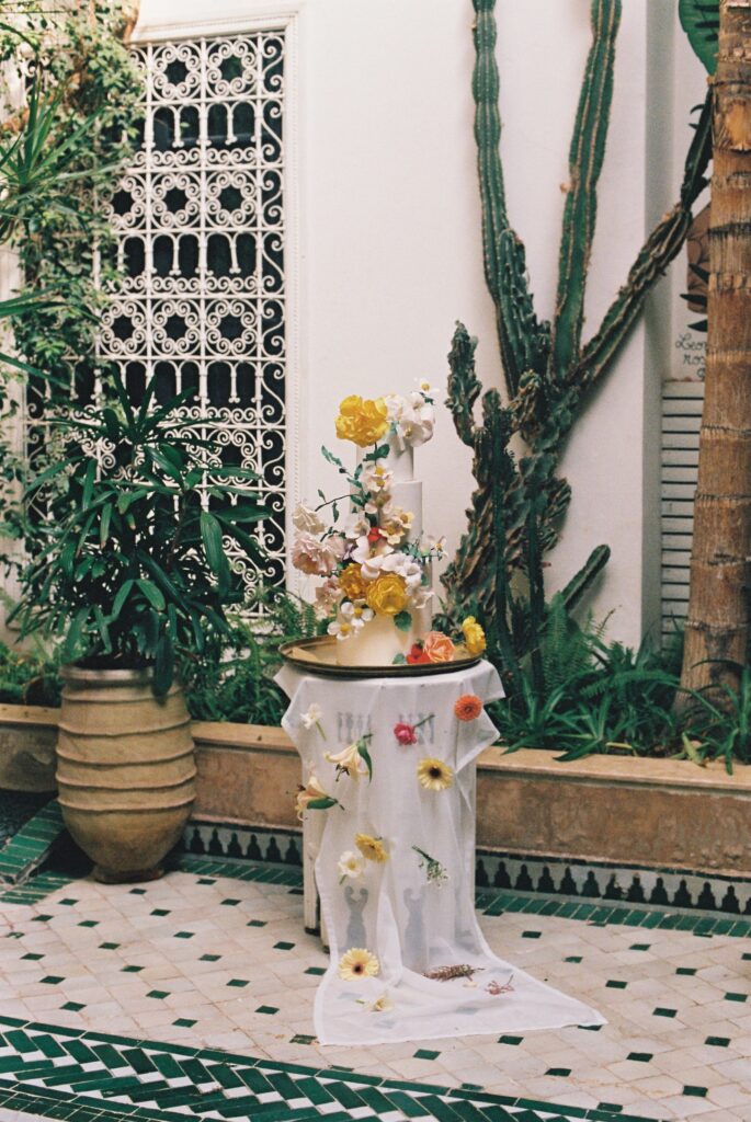 Wedding cake decorated with fresh flowers in a Marrakesh riad courtyard, captured on 35mm film.
