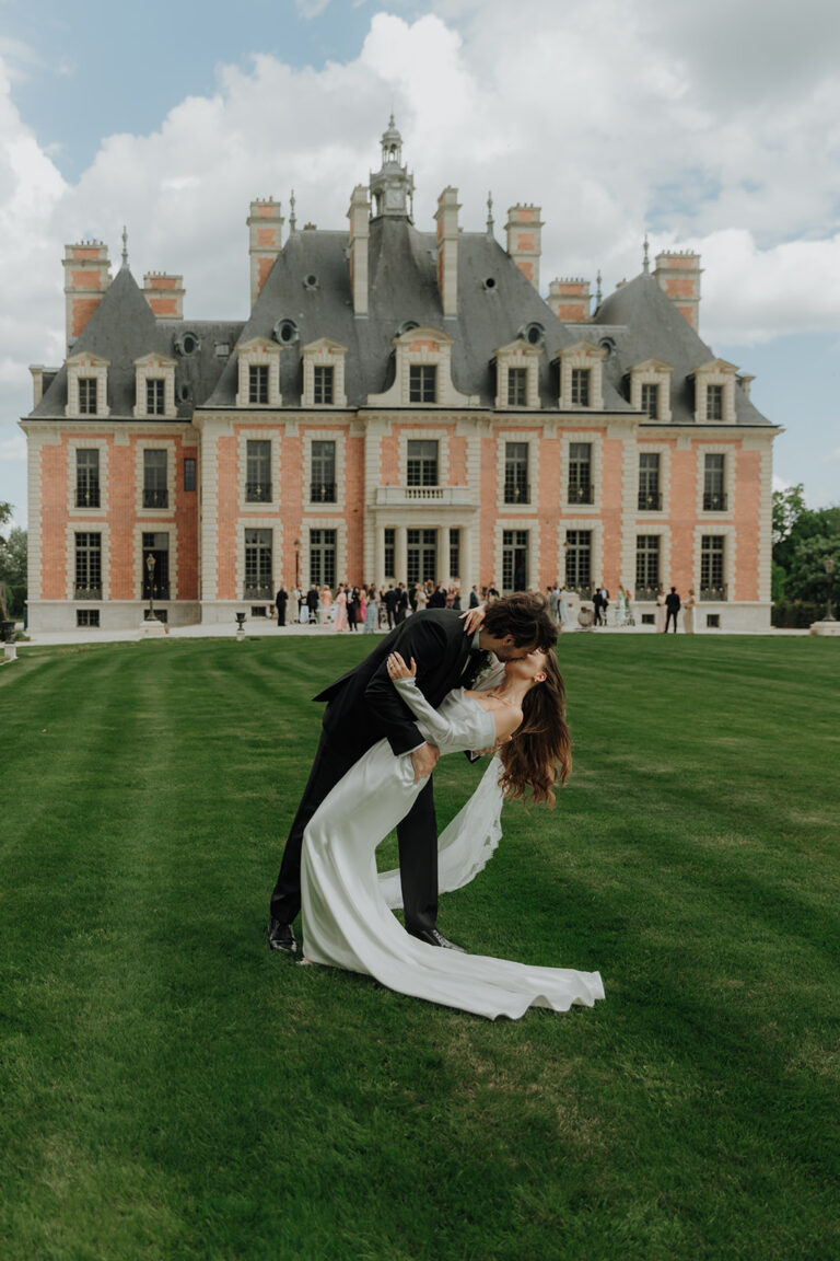 Bride and groom dip kiss in front of a French château on their wedding day
