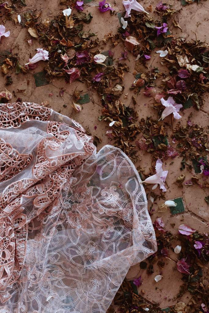 Lace wedding gown laid on Moroccan floor tiles with scattered flower petals