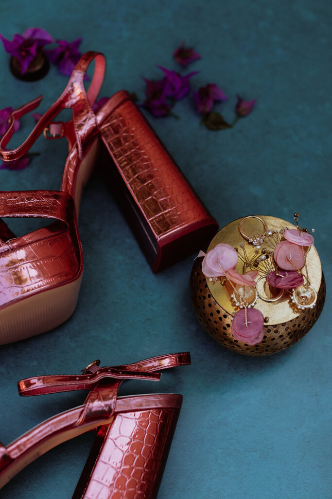 Flat lay of red heels, lipstick, and floral details on wedding morning