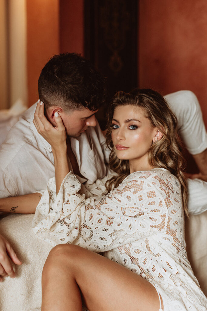 Bride in white lace leaning on groom in Marrakesh bedroom