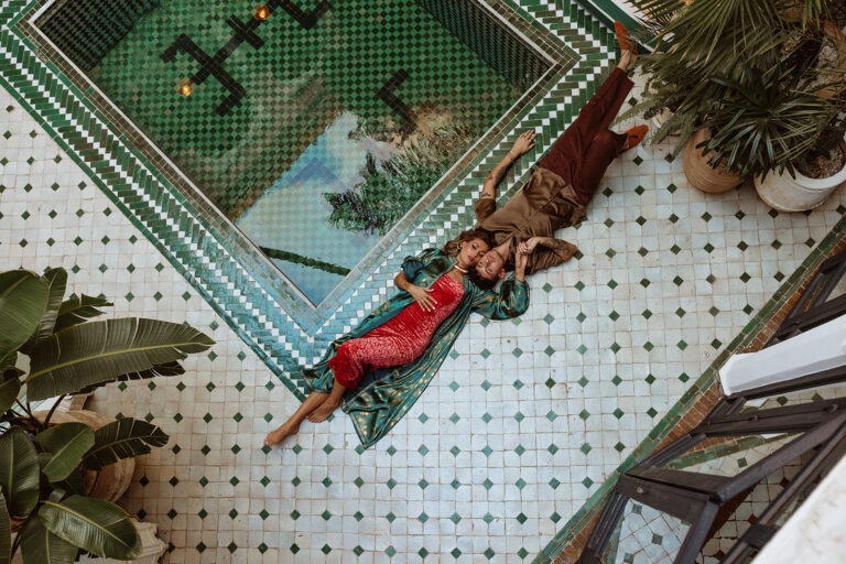 Iconic green-tiled pool with striped loungers and lush plants at Le Riad Yasmine, Marrakesh, with couple