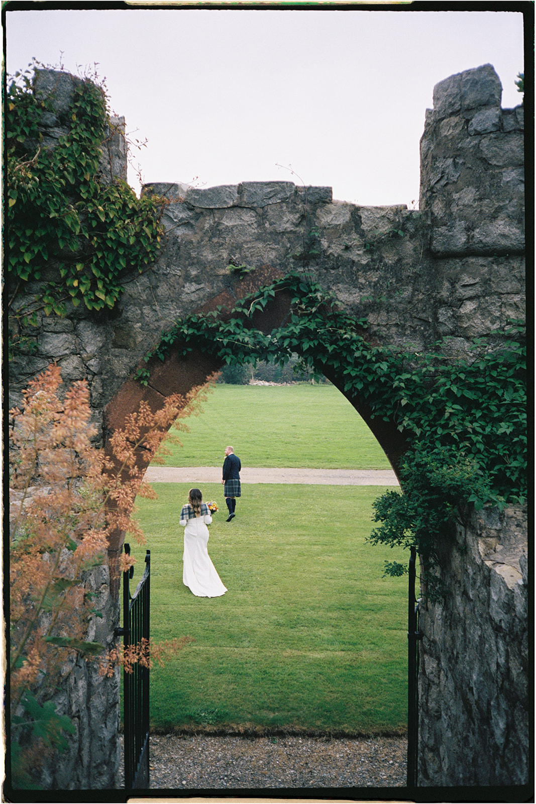 Bride and groom walking through stone archway during Isle of Arran elopement on 35mm film