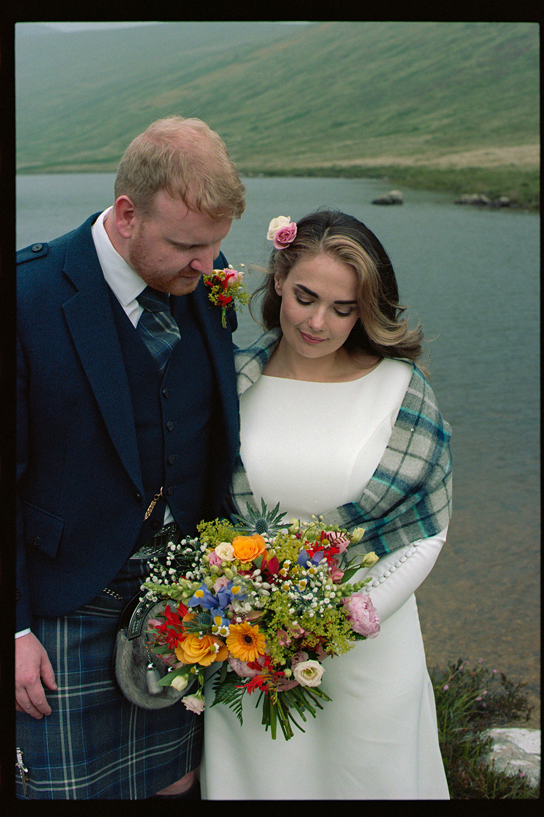 Bride in tartan shawl holding colourful bouquet with groom beside her, Isle of Arran on 35mm film
