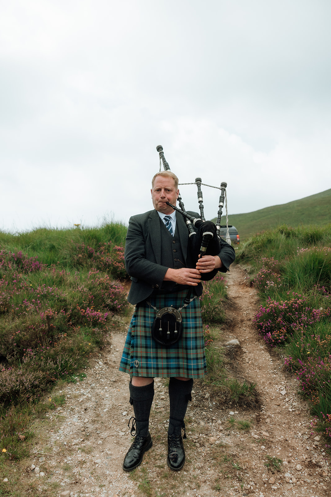 Bagpiper in traditional kilt playing on hillside at Isle of Arran elopement.
