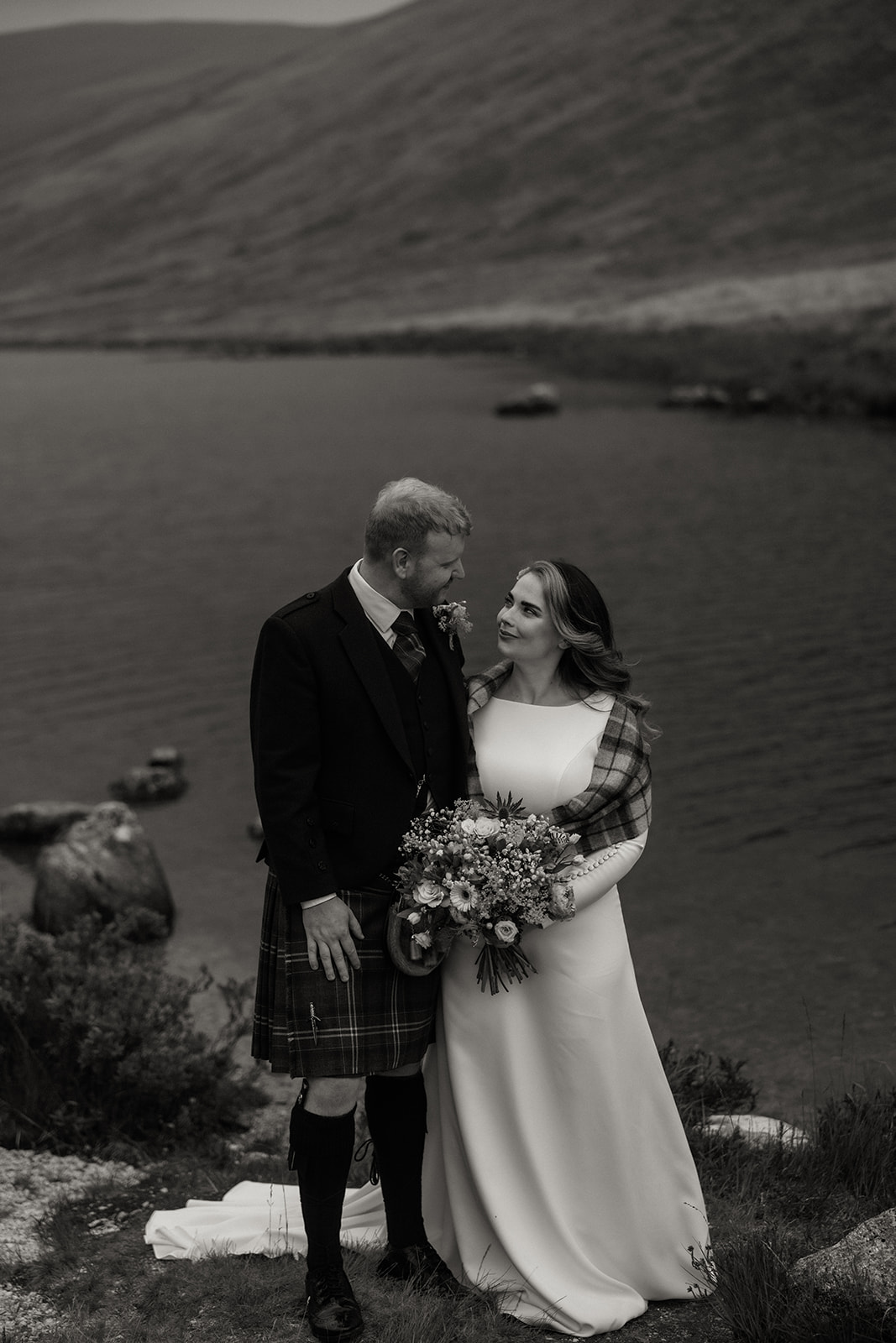 Bride and groom standing close with loch behind during Isle of Arran elopement.