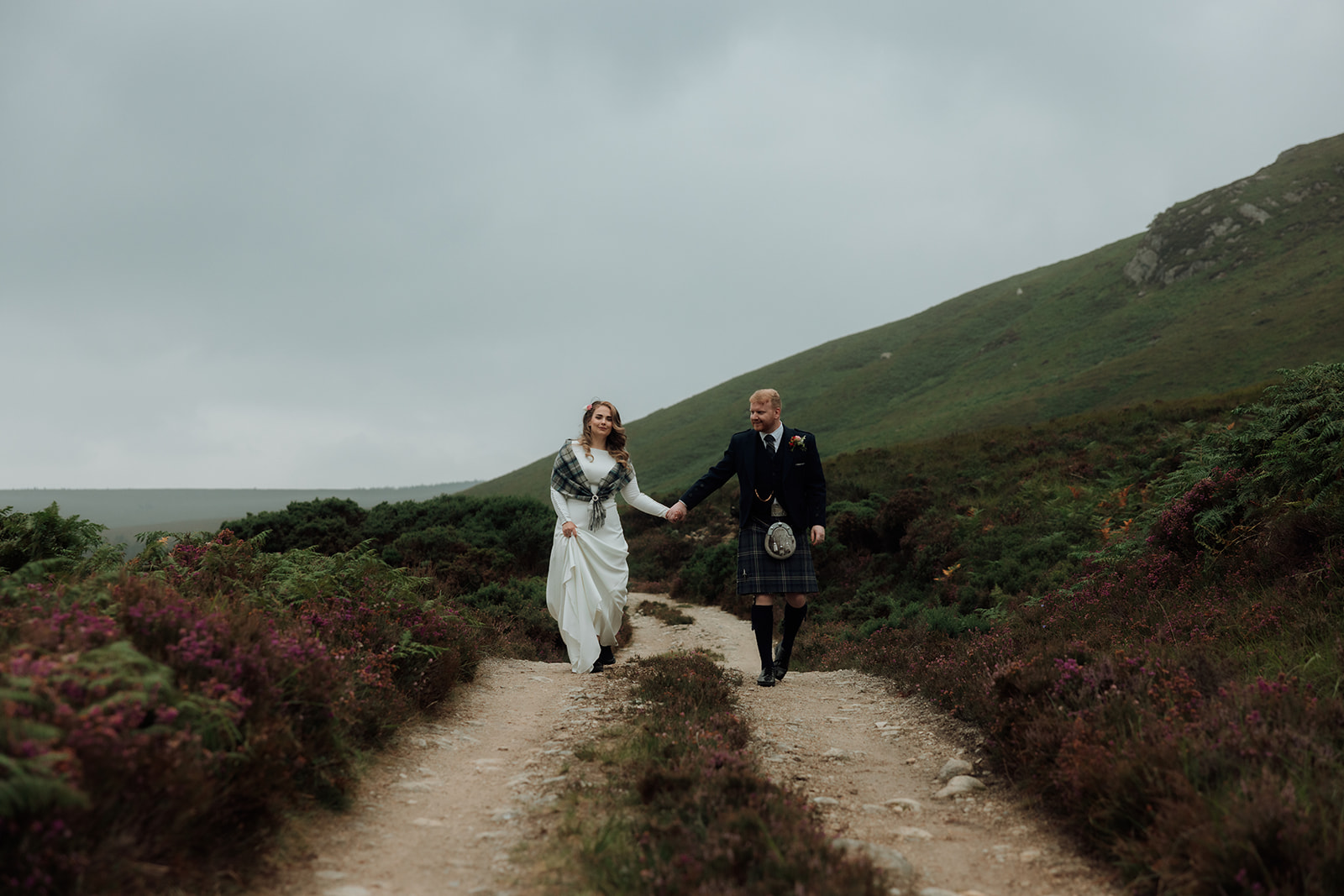 Bride and groom walking along hillside path during Isle of Arran elopement.