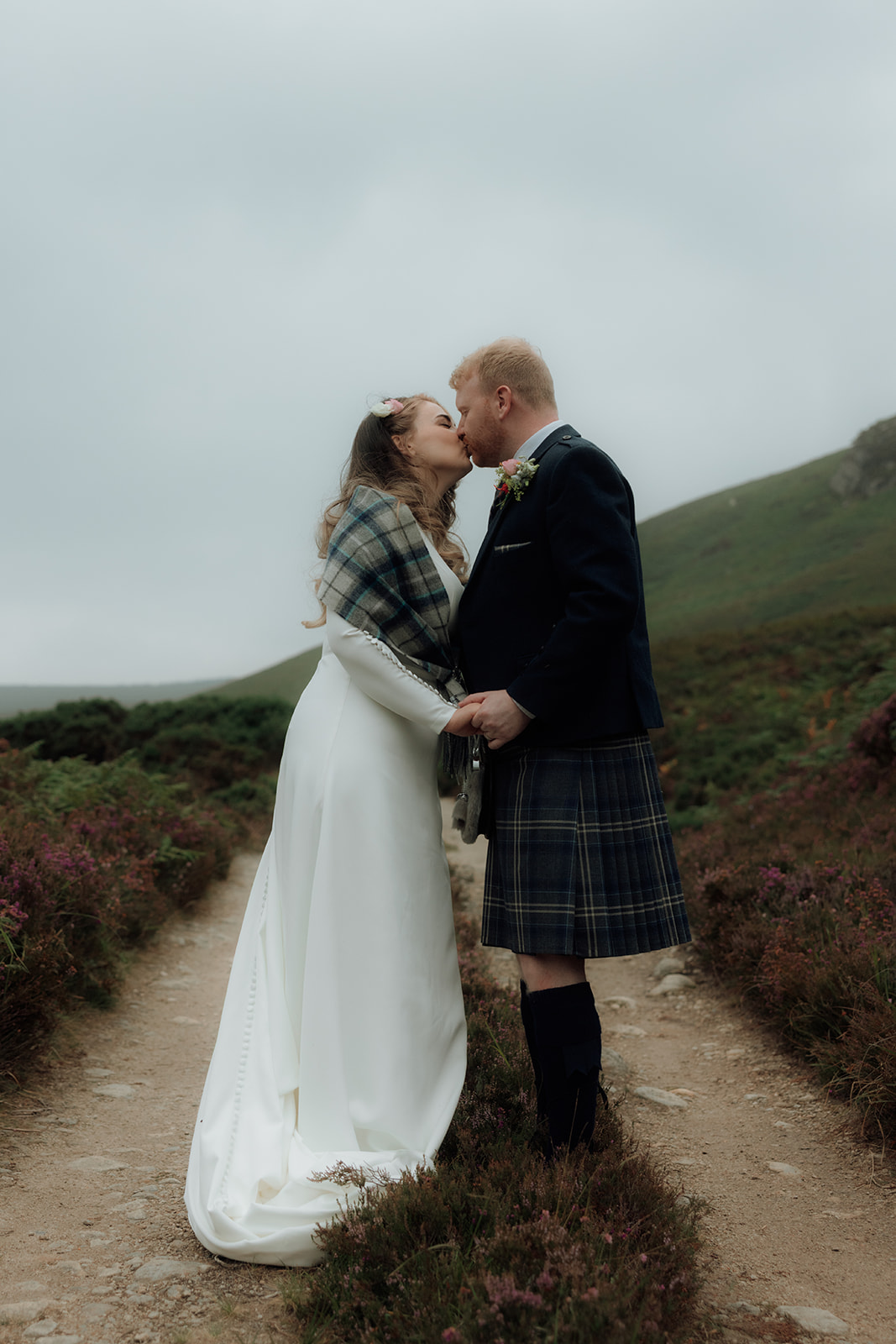 Bride and groom kissing on hillside path during Isle of Arran elopement.