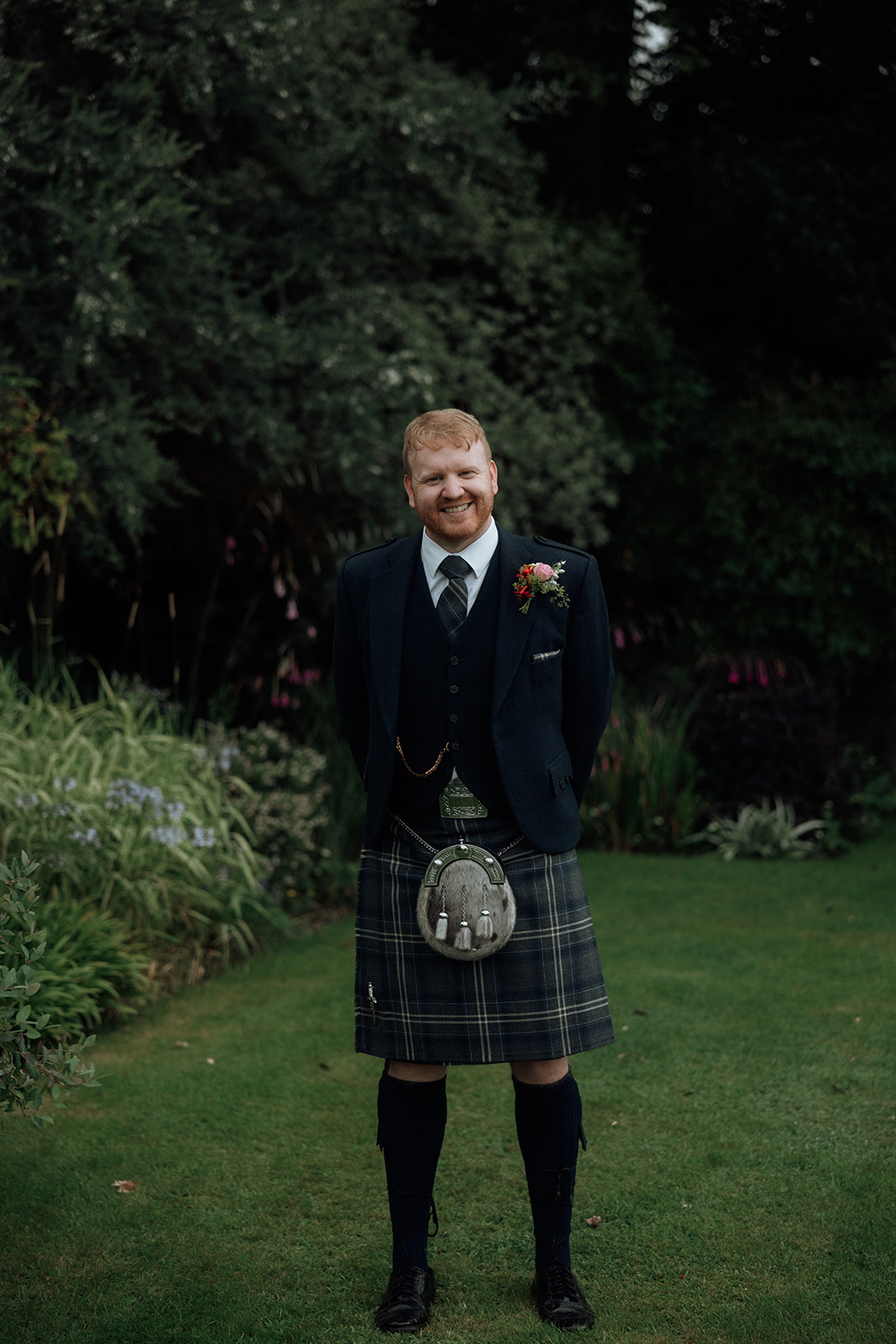 Groom in kilt standing in garden during Isle of Arran elopement.