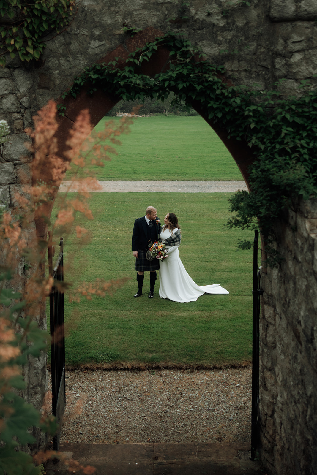 Bride and groom standing together on lawn beneath stone archway during Isle of Arran elopement.