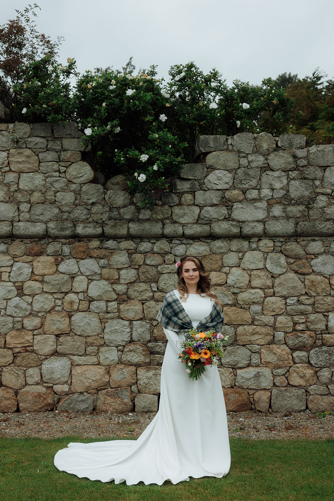Bride holding bouquet standing against stone wall during Isle of Arran elopement.
