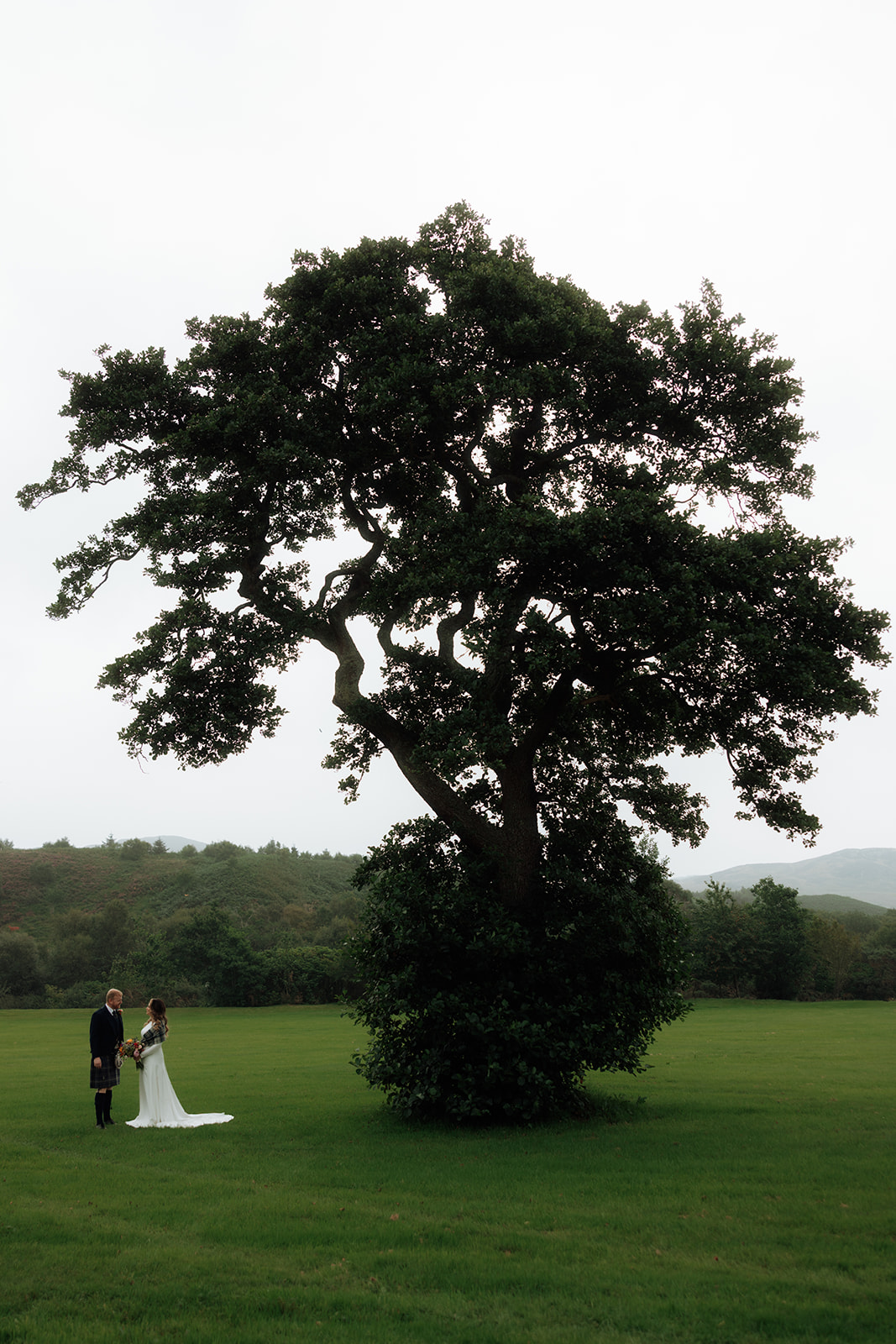 Bride and groom standing beneath large tree during Isle of Arran elopement.