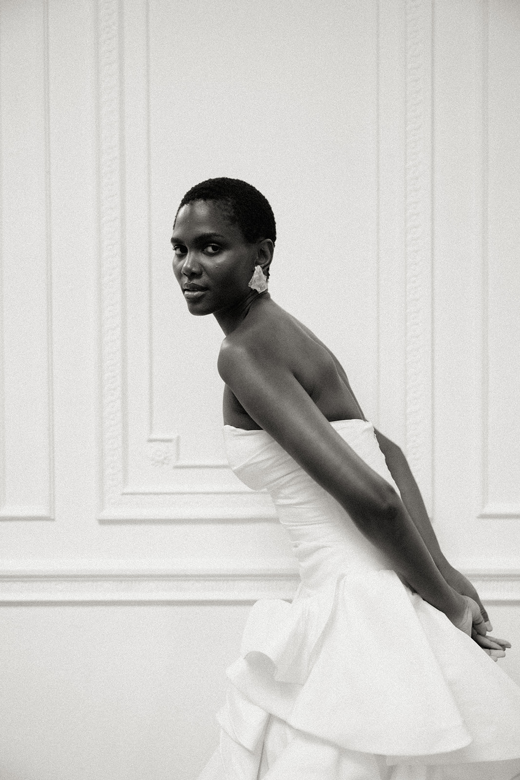 Bride in strapless couture gown standing side profile against panelled wall, editorial bridal portrait.