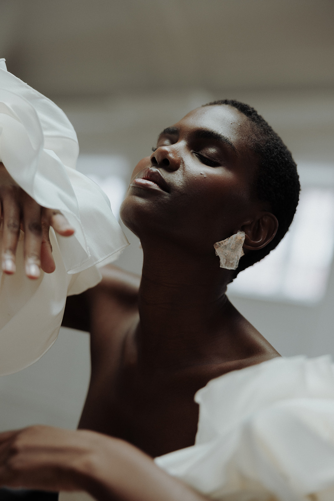 Bride wearing oversized floral earrings in couture gown, editorial bridal portrait.