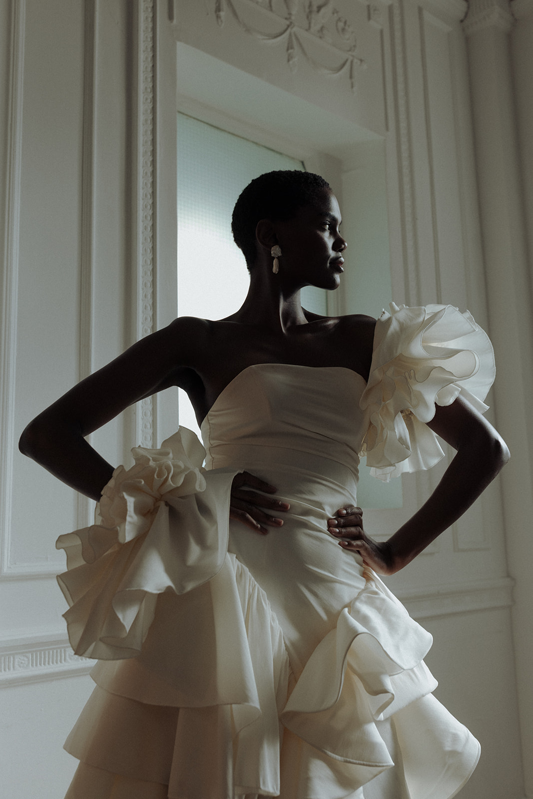 Bride in sculptural Darla Haute Couture gown posing by window, editorial silhouette.