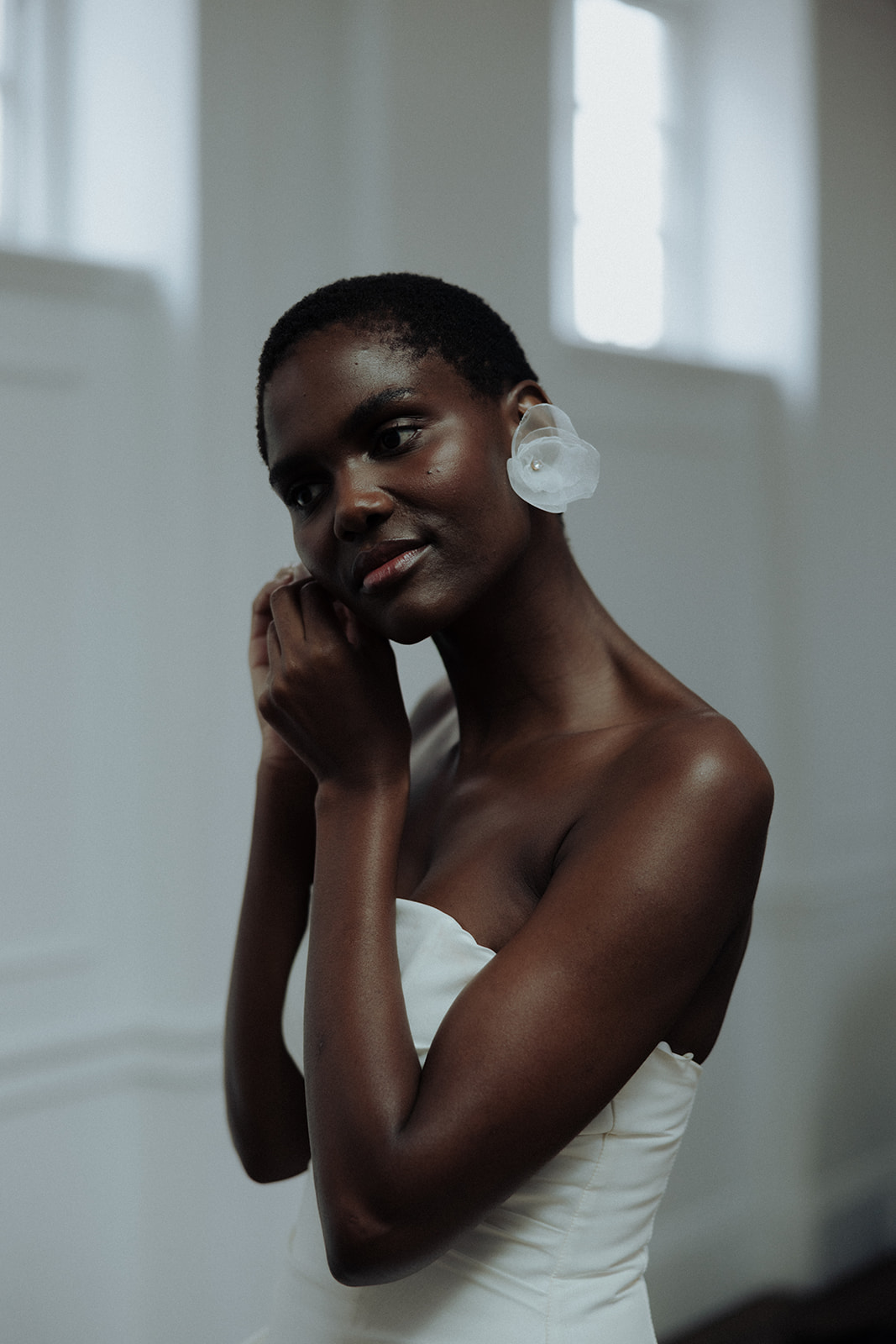 Bride adjusting luminous earrings, close-up editorial bridal photograph.