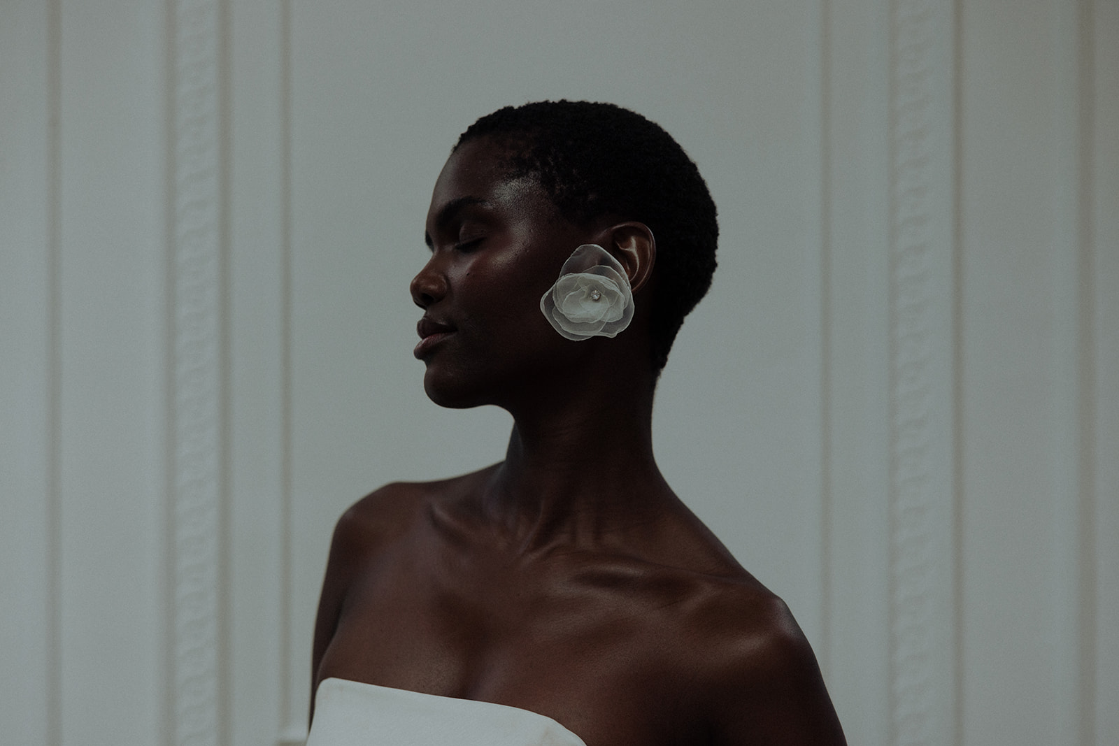 Bride in strapless couture gown wearing oversized floral earrings, editorial bridal portrait.