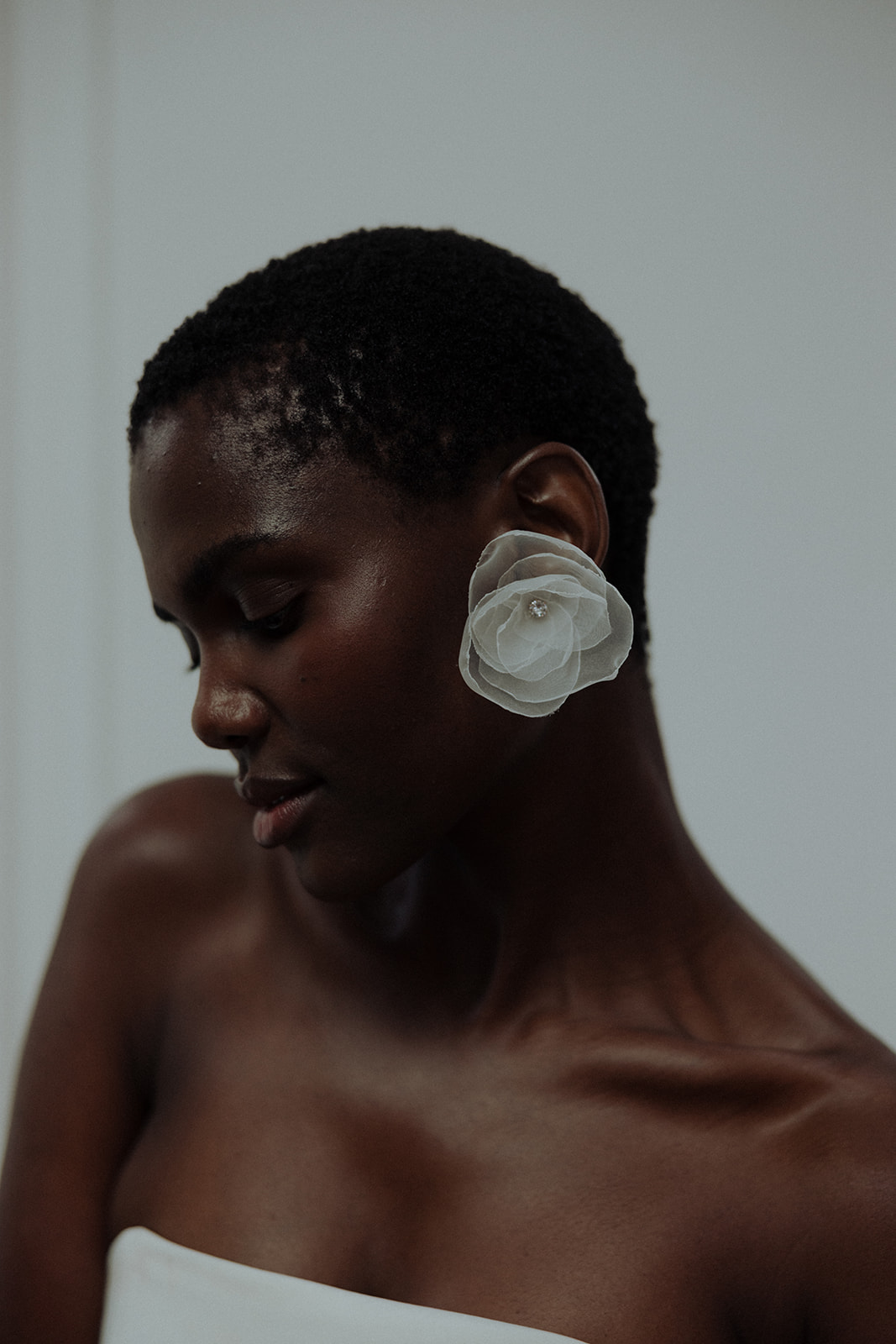 Bride in couture gown wearing sculptural floral earring, close-up editorial portrait.
