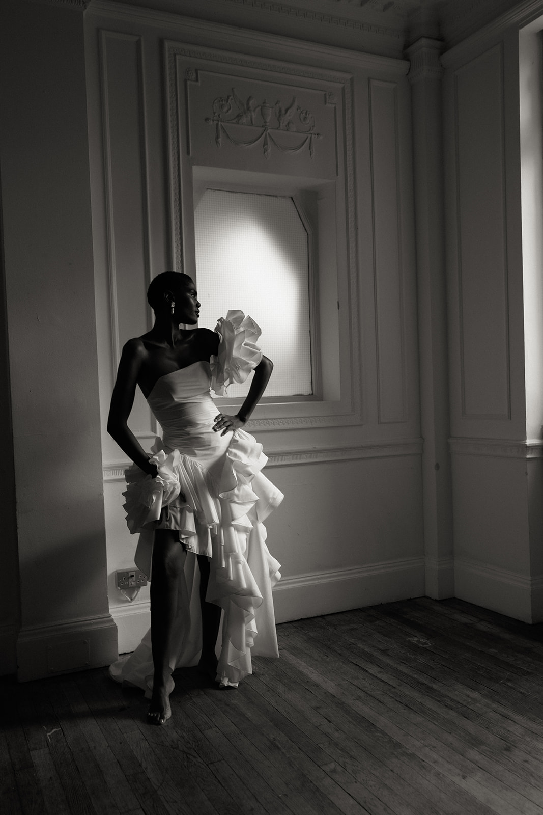 Bride in sculptural Darla Haute Couture gown standing by window, editorial wedding portrait.
