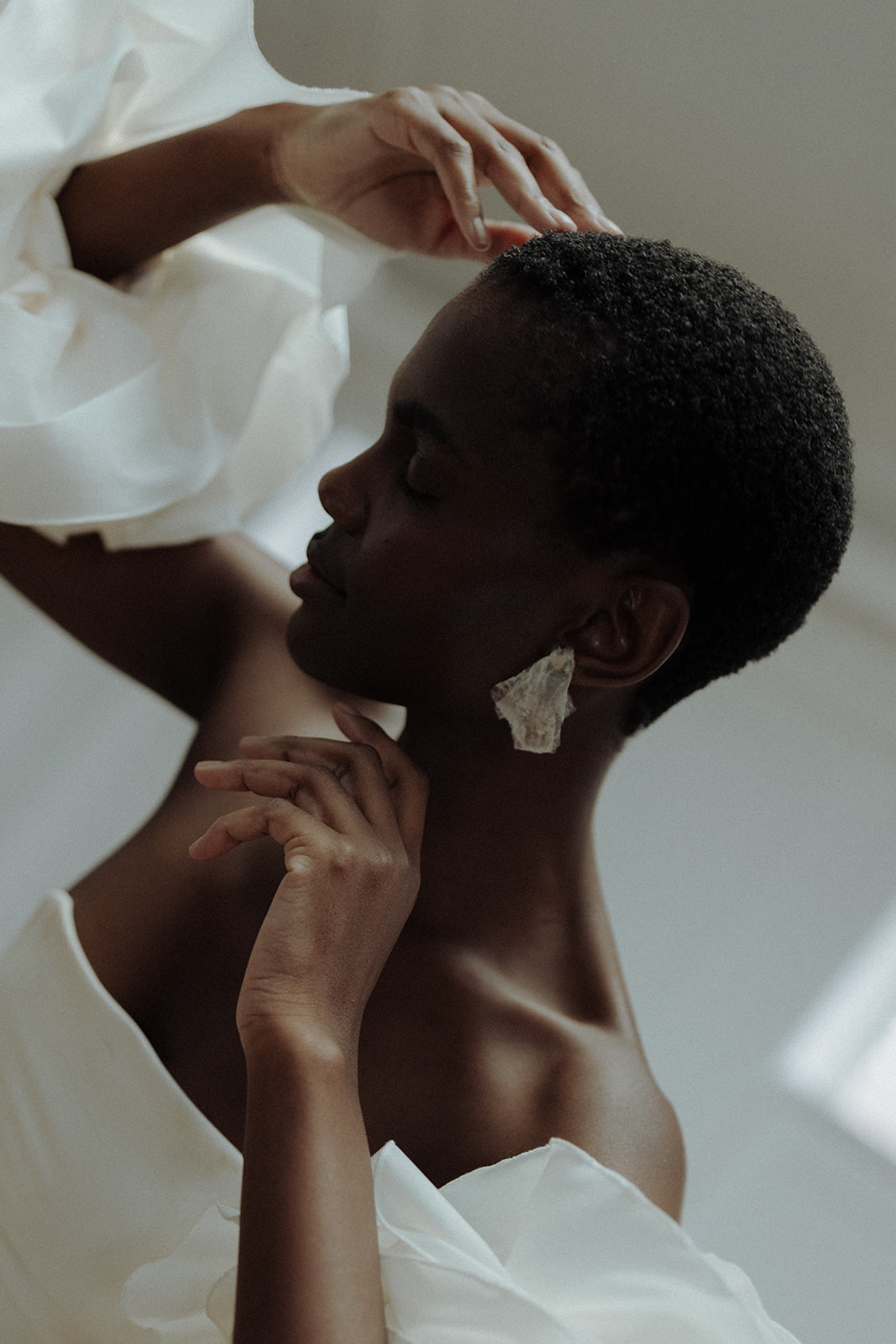 Bride in couture gown with ruffled sleeve and luminous earrings, arms lifted in editorial motion.