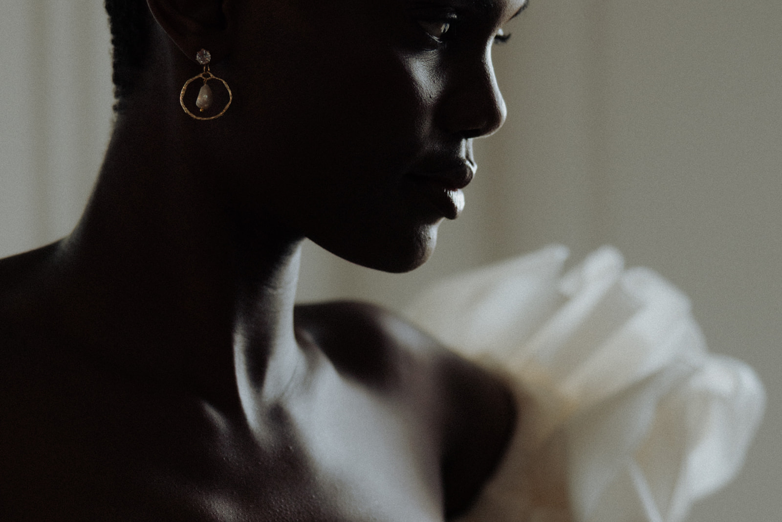 Bride in couture gown with ruffled sleeve seated at window, editorial bridal portrait.